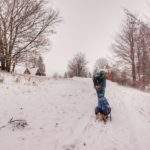 Mężczyzna ciągnący na sankach dziecko - Przełęcz Przysłop Potócki, w oddali widoczne drewniane chatki bazy namiotowej, zimowe warunki