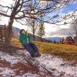 Szczęśliwe dziecko na huśtawce przymocowanej do drzewa, w tle studencka baza namiotowa Przysłop Potócki