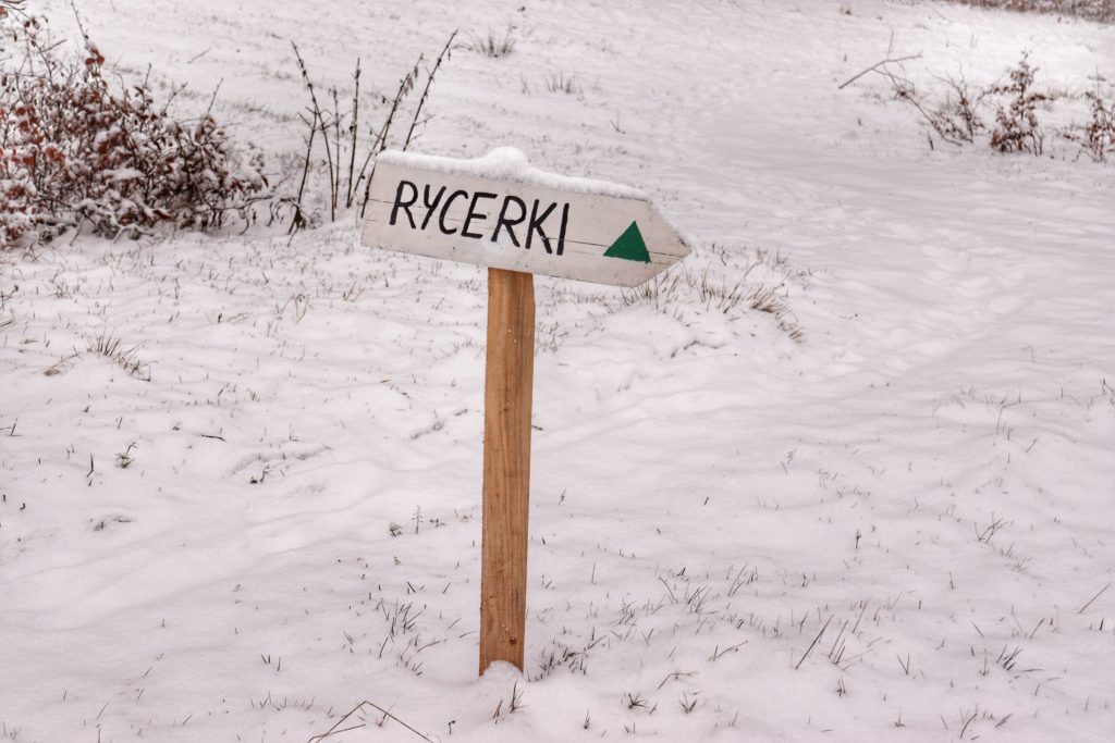 Tabliczka w kształcie strzałki z napisem Rycerki, zielony szlak bazowy, śnieg