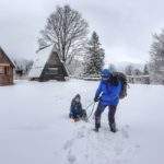 Turysta ciągnący dziecko na sankach - Przełęcz Przysłop Potócki, w tle widoczne drewniane chatki studenckiej bazy noclegowej