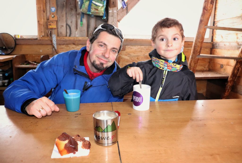 Turysta z dzieckiem siedzący przy stole w drewnianej chatce - baza noclegowa Przysłop Potócki