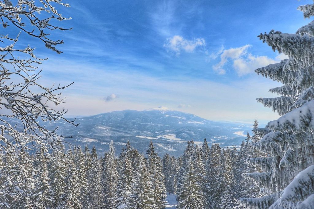 Widok na najwyższy szczyt Beskidu Żywieckiego Babią Górę, która jest pokryta śniegiem z niebieskiego szlaku na Pilsko, zima, niebieskie niebo