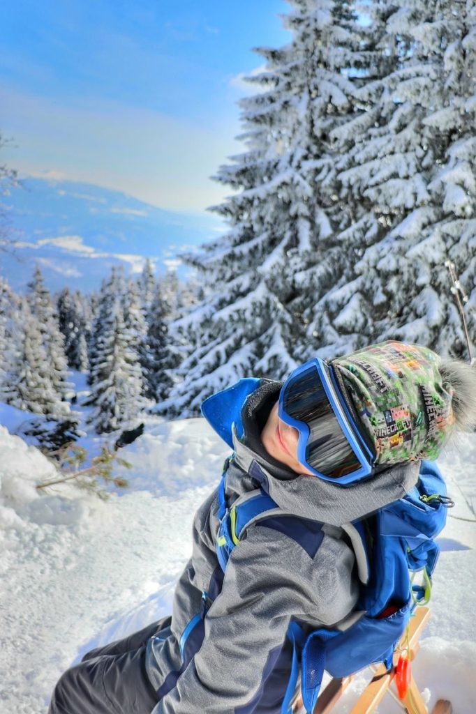 Zadowolone dziecko odpoczywające na drewnianych sankach na szlaku idącym na Pilsko z Przełęczy Glinne, zima, drzewa pokryte śniegiem