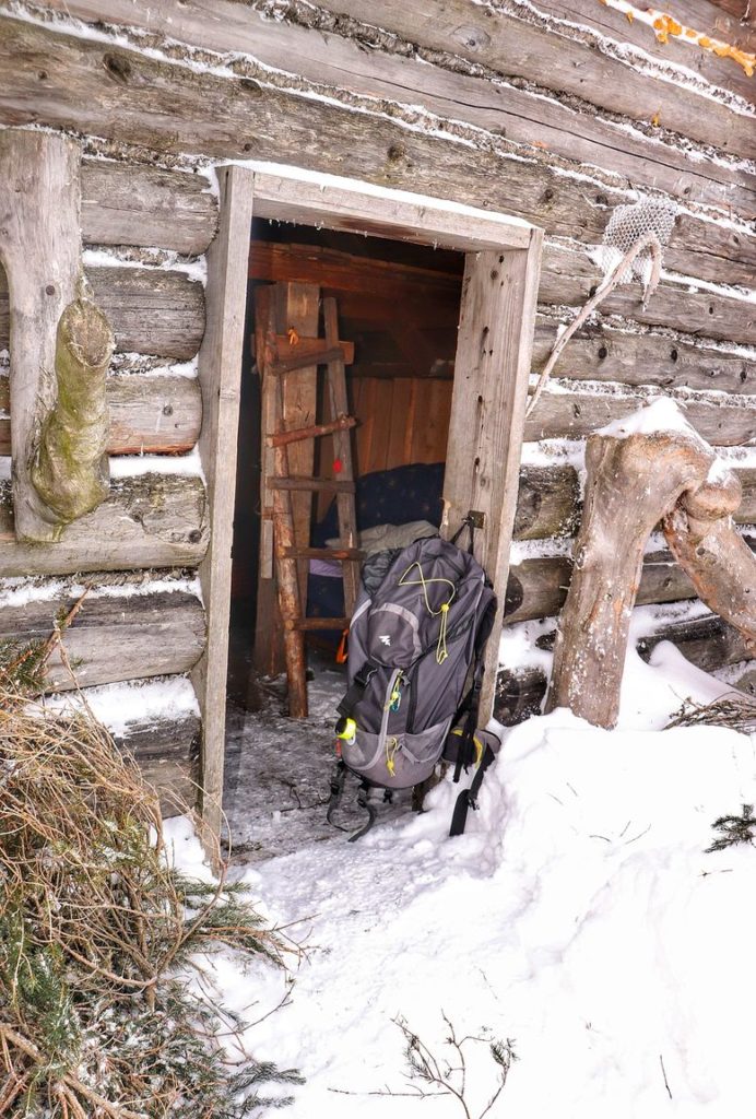 Drewniana chata na Hali Baraniej, otwarte drzwi, oparty o futrynę plecak turystyczny, zima