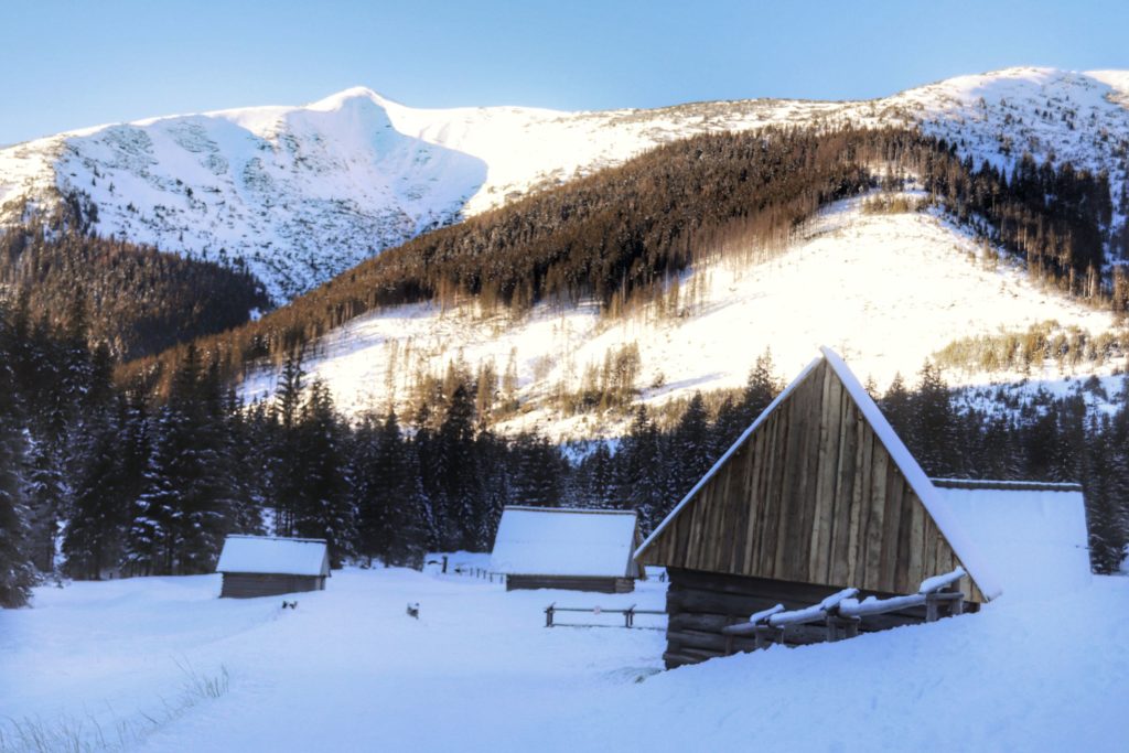 Drewniane chatki na Polanie Chochołowskiej, zimowa pora, zaśnieżone tatrzańskie szczyty