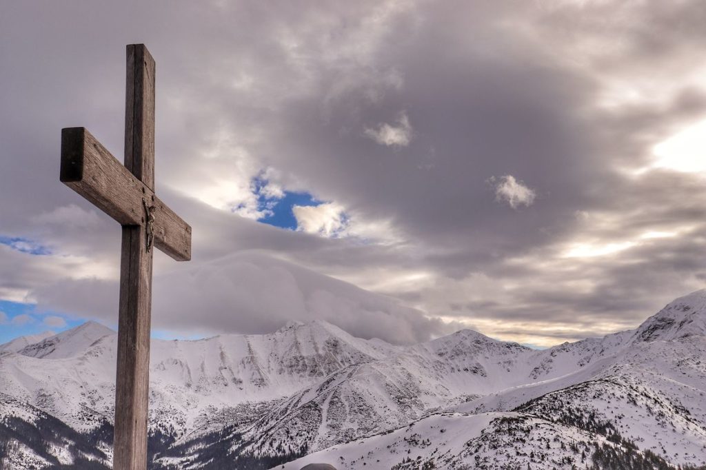 Drewniany krzyż stojący na szczycie Grześ, w tle zimowe tatrzańskie szczyty, zachmurzone niebo