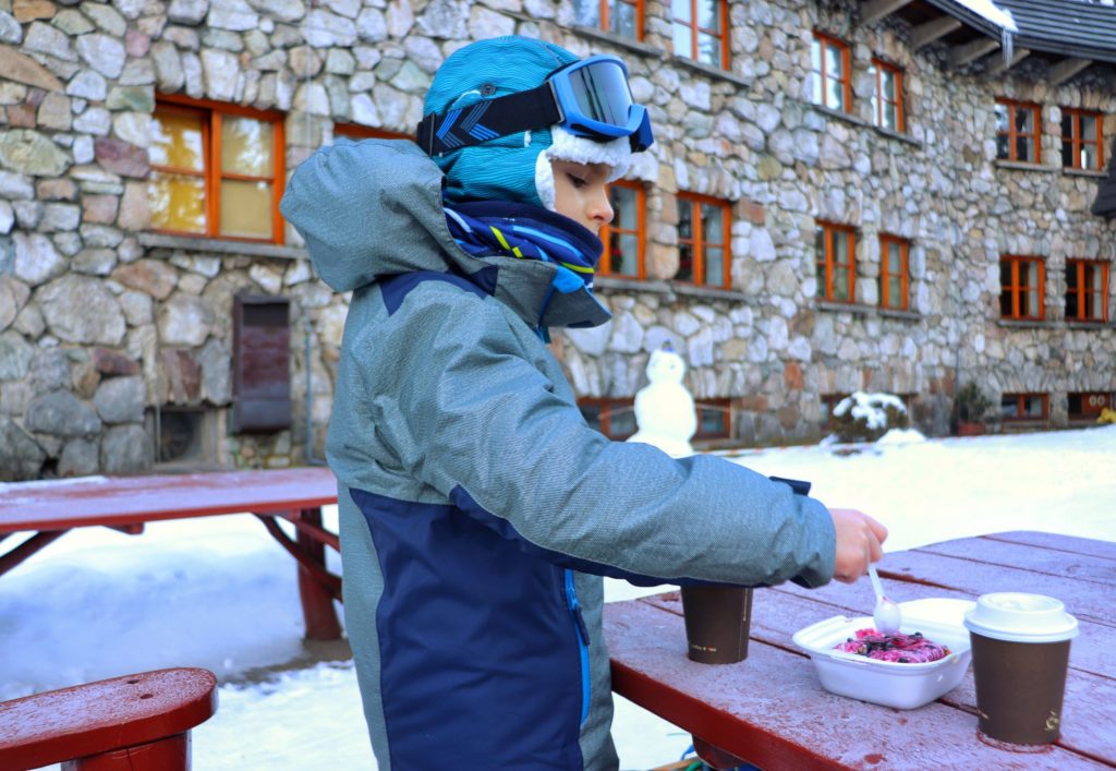 Dziecko wcinające Deser Chochołowski przed budynkiem schroniska w Dolinie Chochołowskiej, zima