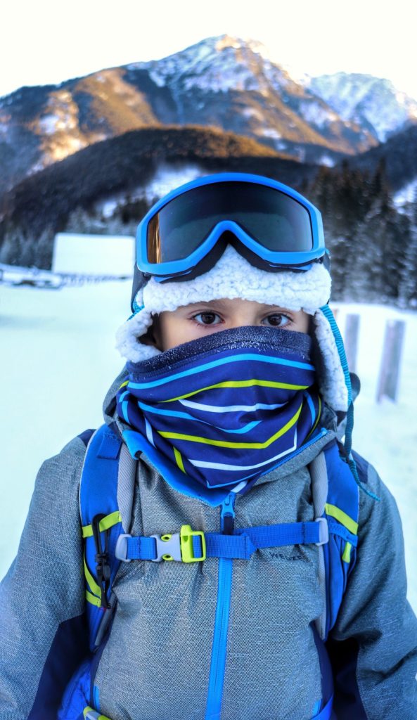 Dziecko zimą na Polanie Chochołowskiej z naciągniętym na twarz kominem, w tle tatrzański szczyt