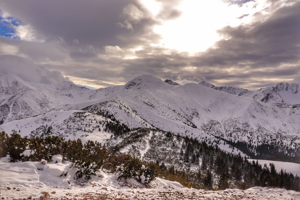 Krajobraz widziany ze szczytu Grześ, zaśnieżone tatrzańskie szczyty, zachmurzone niebo oświetlone przez słońce