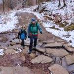 Mężczyzna z dzieckiem przechodzący przez potok przepływający po czarnym szlaku w Beskidzie Małym