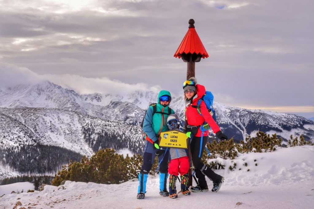 Szczęśliwa, trzyosobowa rodzina (z dzieckiem) na szczycie Grześ w Tatrach Zachodnich, zima, w tle pokryte śniegiem tatrzańskie szczyty, zachmurzone niebo