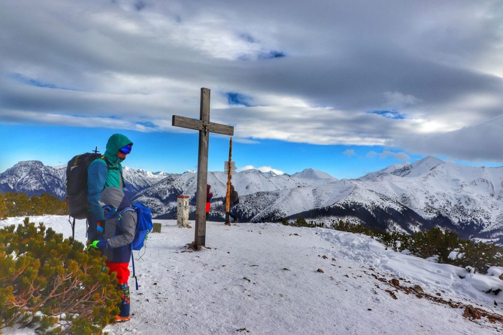 Turyści, drewniany krzyż na szczycie Grześ, zimowy krajobraz - widok na ośnieżone Tatry