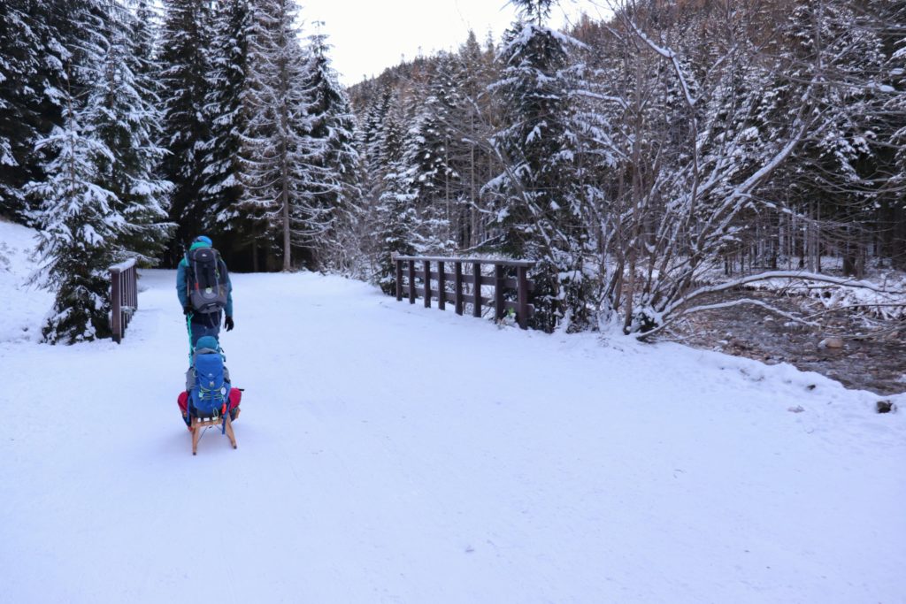 Turysta, dziecko na sankach, zielony szlak w Dolinie Chochołowskiej, most, zima