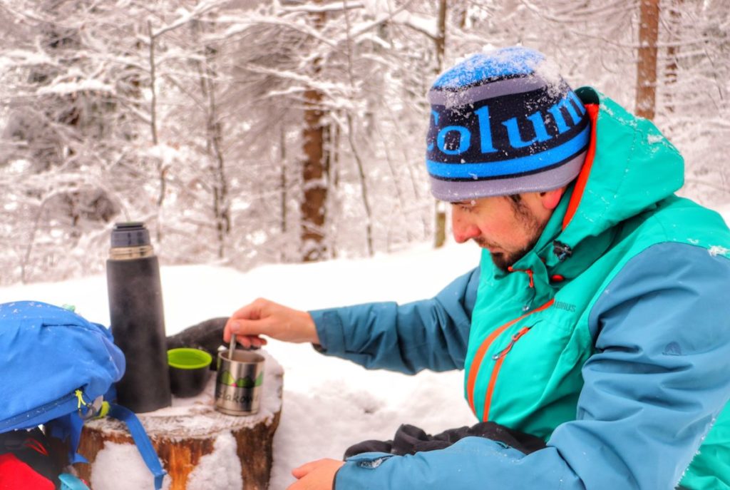 Turysta odpoczywający na szlaku w Beskidzie Małym, zima, las, kubek z kawą, termos z ciepłą wodą