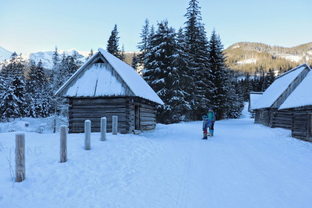 Turysta z dzieckiem na Polanie Chochołowskiej zimą, drewniane szałasy