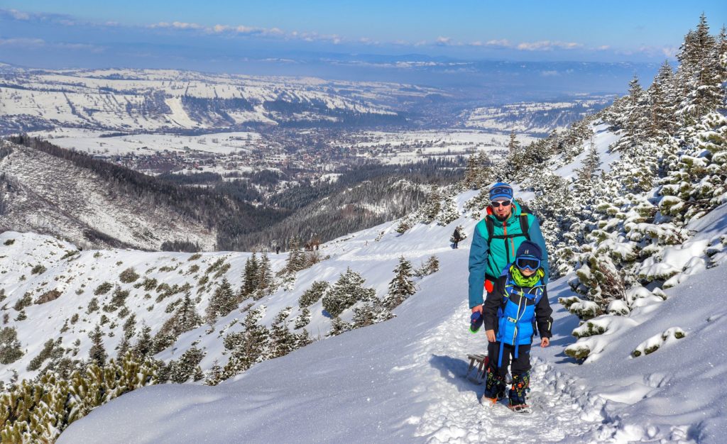 Turysta z dzieckiem pokonuje ostatnie podejście na niebieskim szlaku z Kuźnic do Przełęczy między Kopami, w koło zimowy krajobraz