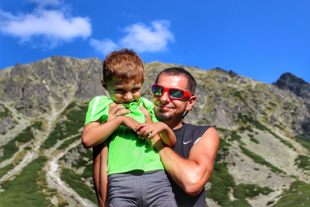 Turysta ze szczęśliwym dzieckiem na rękach na tle Tatr Wysokich nad Czarnym Stawem Gąsienicowym, niebieskie niebo