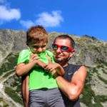 Turysta ze szczęśliwym dzieckiem na rękach na tle Tatr Wysokich nad Czarnym Stawem Gąsienicowym, niebieskie niebo