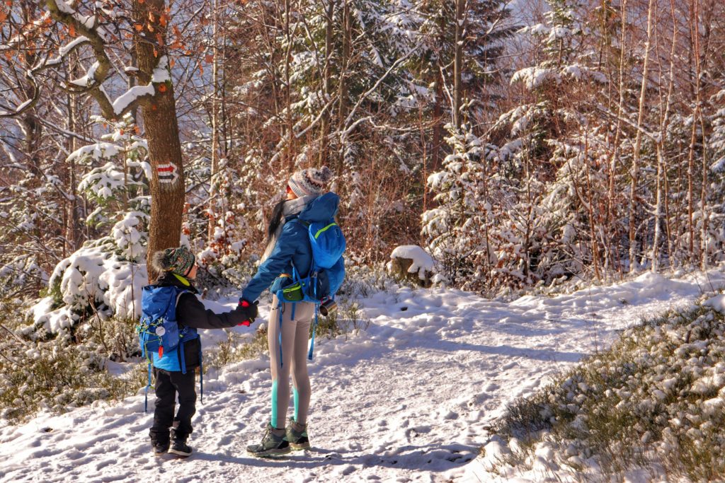 Turystka z dzieckiem na czerwono - czarnym szlaku idącym do Chatki na Rogaczu, zima, zaśnieżona ścieżka oraz drzewa
