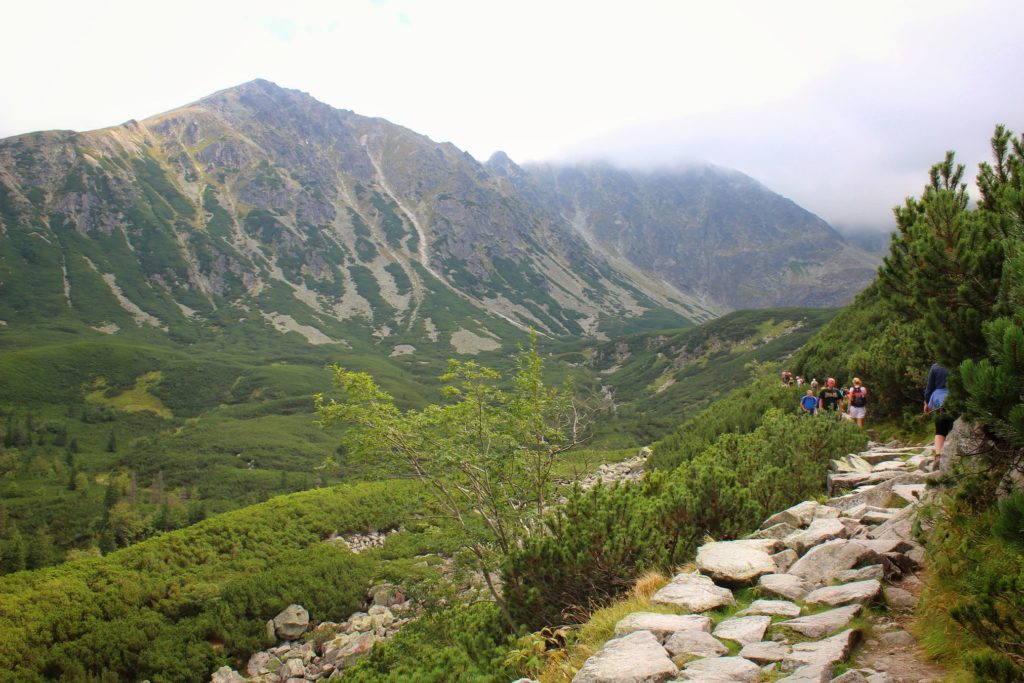 Wąski, skalny chodnik na niebieskim szlaku idącym nad Czarny Staw Gąsienicowy, w oddali turyści, tatrzańskie szczyty, ciężkie chmury