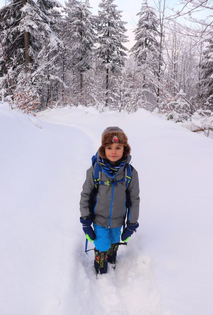 Zadowolone dziecko idące w głębokim śniegu, ośnieżone drzewa