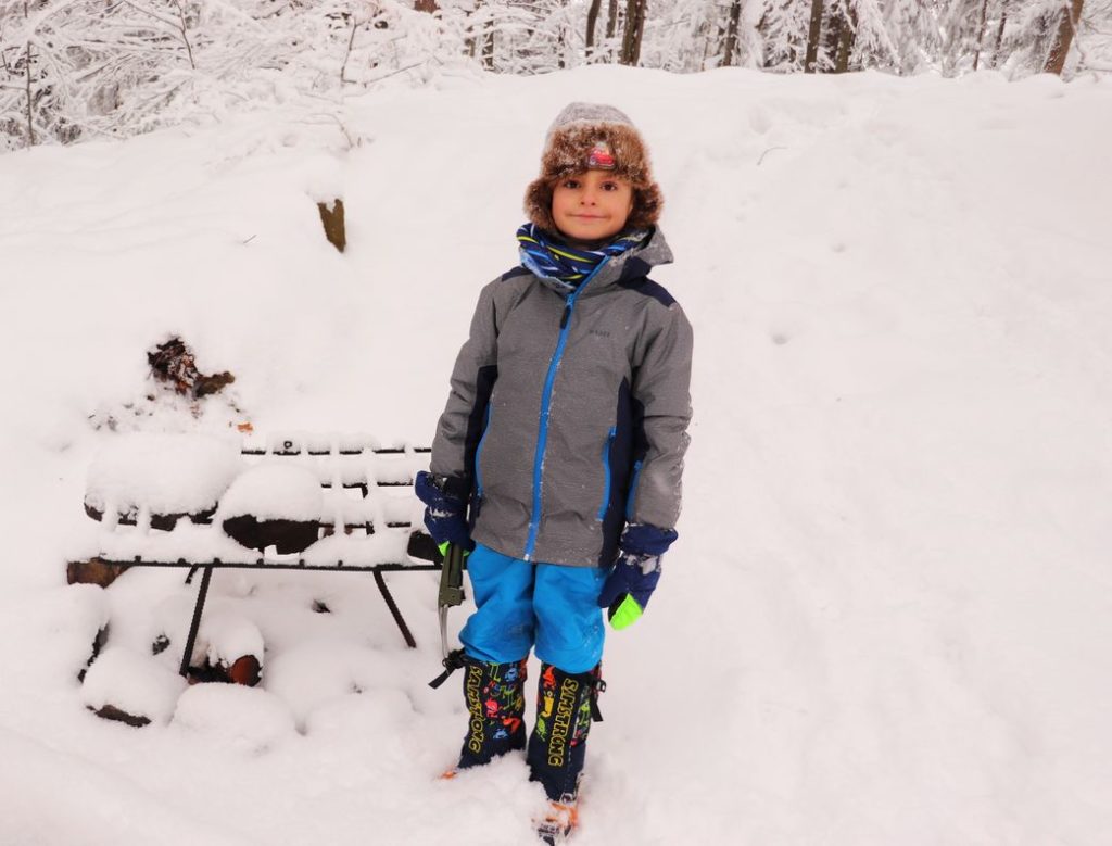 Zadowolone dziecko stojące obok metalowego grilla w okolicach szczytu Gaiki, zima
