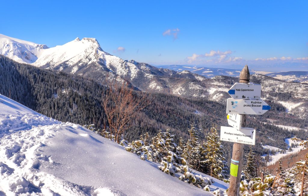 Zima, Przełęcz między Kopami, słup z białymi tabliczkami na tle zaśnieżonego Giewontu