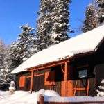 Drewniany budynek w Kamesznicy pokryty warstwą śniegu - Ostoia pod Jodłą u podnóża Baraniej Góry, zaśnieżone drzewa na tle błękitnego nieba