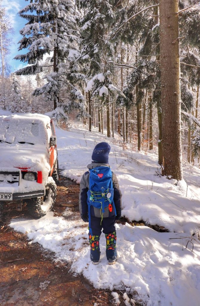 Droga leśna, śnieg, potok, mężczyzna z dzieckiem na sankach, czerwony samochód zaparkowany w lesie na niebieskim szlaku idącym na Halę Boraczą z Rajczy