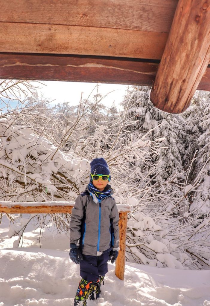 Dziecko stojące pod drewnianym dachem chatki Sucha Góra, zima