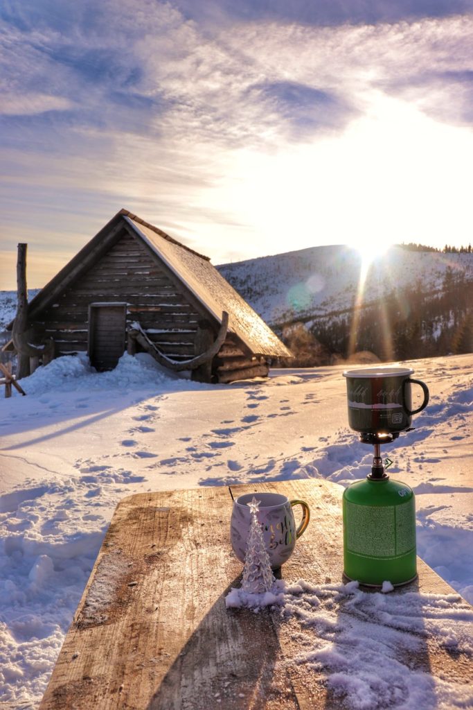 Hala Barania zimą, zachodzące słońce, drewniana chatka, drewniany stół stojący przed chatą, butla gazowa, kubki