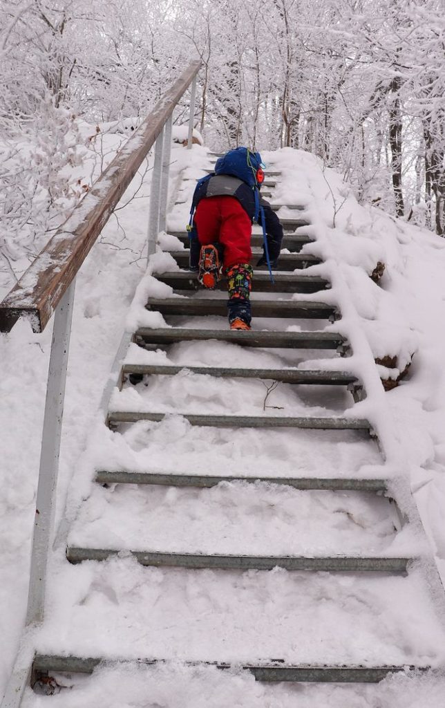 Metalowe schody pokryte śniegiem na niebieskim szlaku na Wysoką w Pieninach, dziecko wspinające się po tych schodach, zima