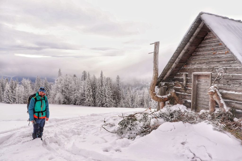 Piękna, zaśnieżona Hala Barania, turysta stojący obok drewnianej chaty - Bacówki na Hali Baraniej