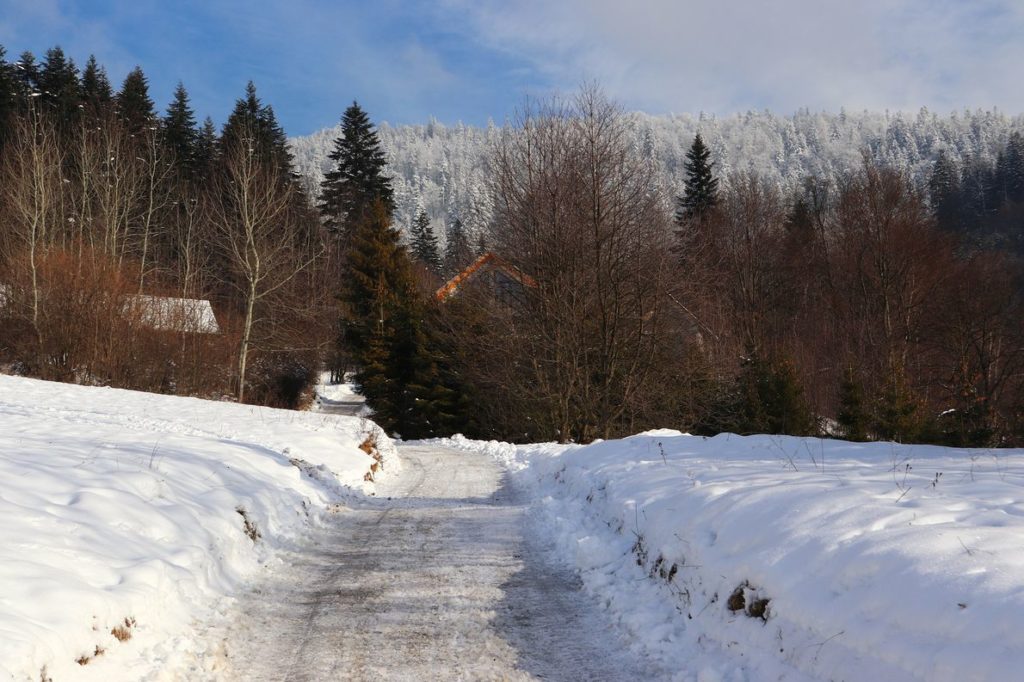 Szeroka droga na niebieskim szlaku w Rajczy pokryta śniegiem, w tle dom, białe od śniegu drzew