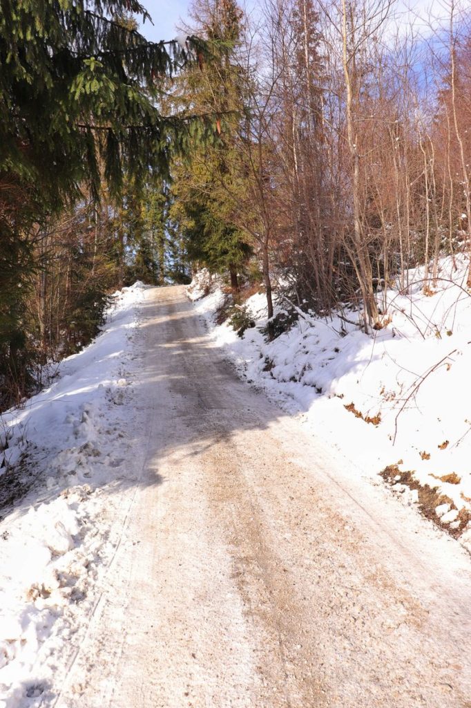 Szeroka, pokryta śniegiem droga we wsi Rajcza na niebieskim szlaku, słoneczny, zimowy dzień