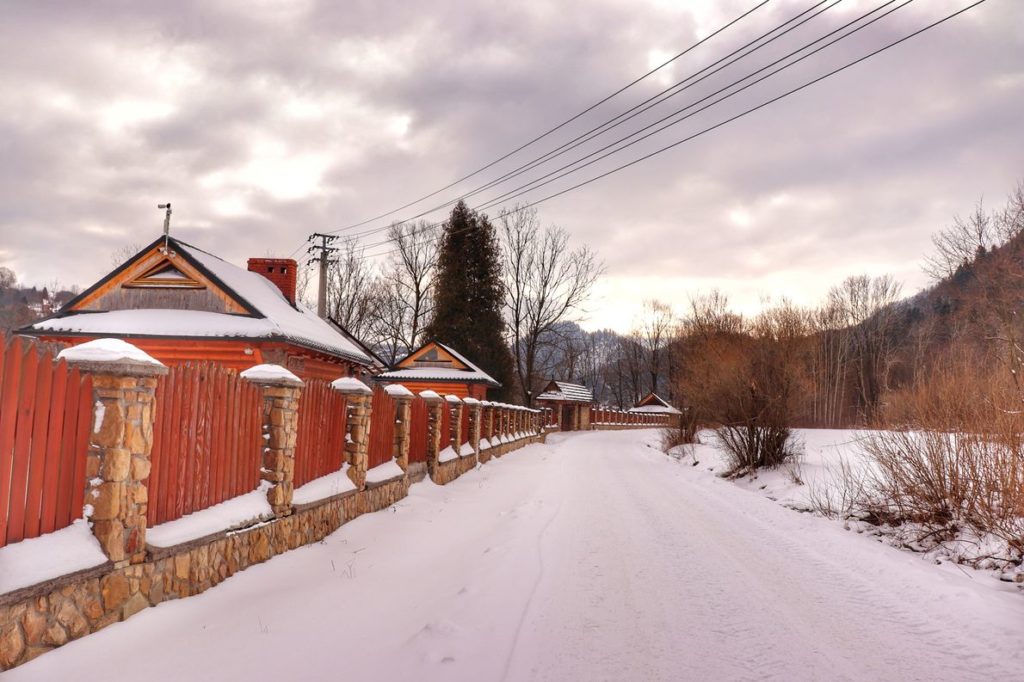 Szeroka, zaśnieżona droga na zielonym szlaku w Krościenku na Sokolicę, po lewej stronie zabudowania, zachmurzone niebo
