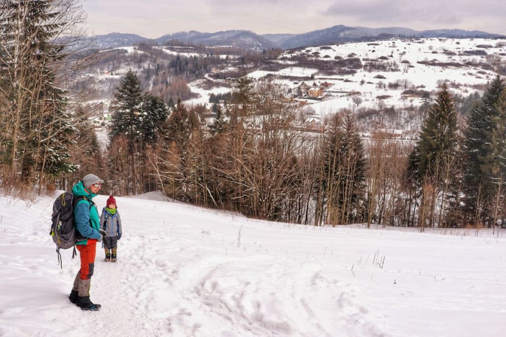 Turysta idący zimą zielonym szlakiem w kierunku Sokolicy podziwiający widoki rozciągające się z Polany - Pod Natonia