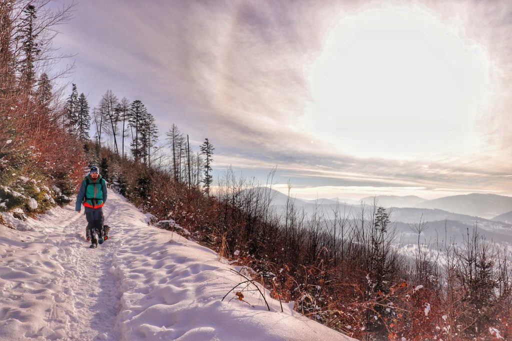 Turysta na szerokiej, zaśnieżonej drodze na niebieskim szlaku w Rajczy - punkt widokowy, na niebie pełne słońce