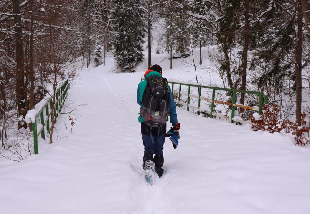 Turysta przechodzący przez most, na którym zalega sporo śniegu, za mostem odejście na drogę pożarową numer W-17 w Kamesznicy