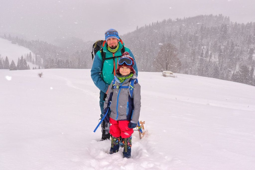 Turysta z uśmiechniętym dzieckiem na zielonym szlaku idącym na Wysoką, zaśnieżona Polana pod Wysoką, dużo śniegu, w tle przyczepa kempingowa 