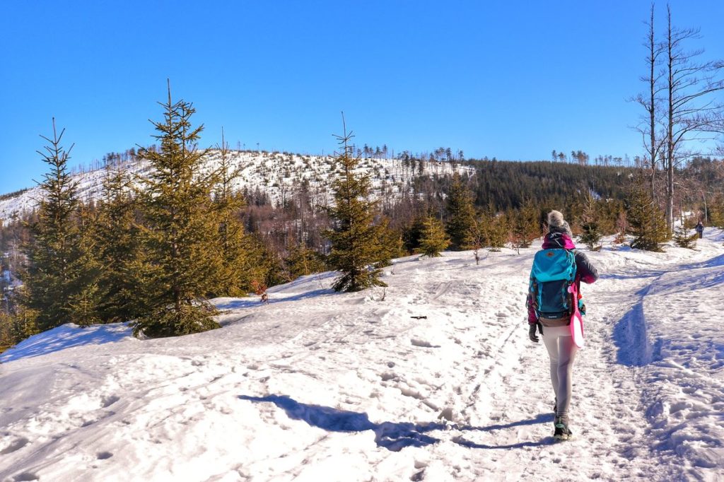 Turystka idąca pokrytą warstwą śniegu ścieżką w stronę Malinowskiej Skały, piękny, słoneczny dzień