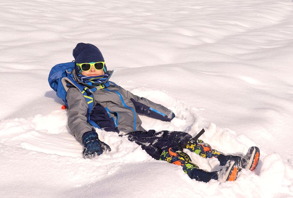 Uśmiechnięte dziecko - chłopiec leżący w śniegu