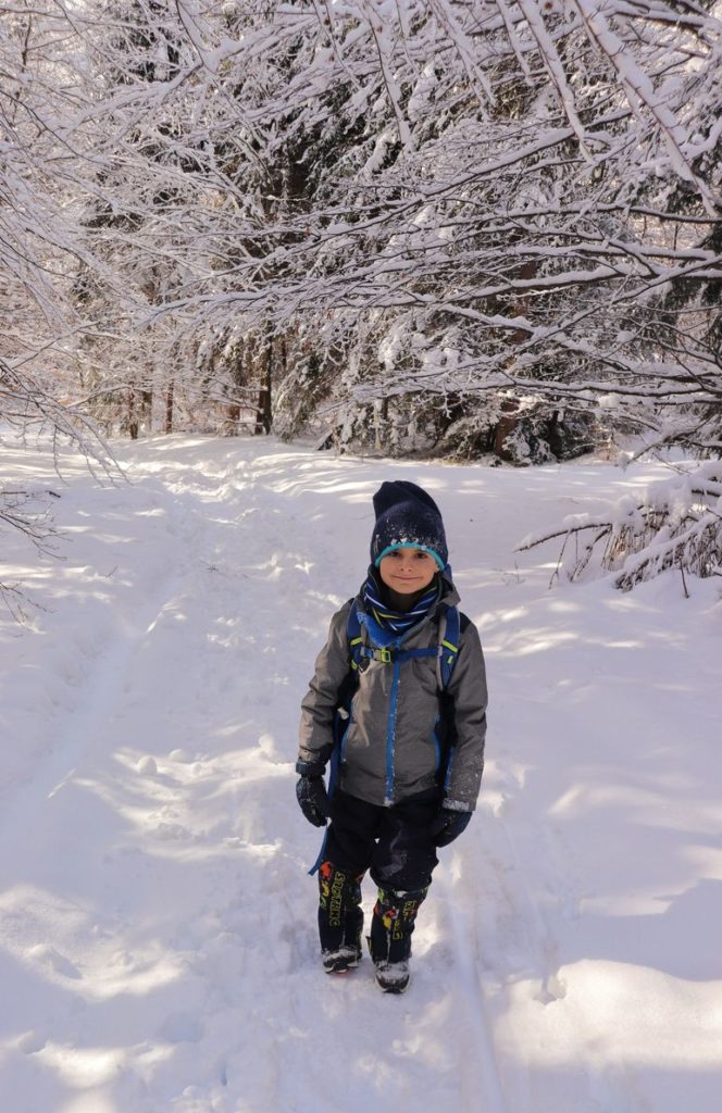 Uśmiechnięte dziecko idące lasem - zimową porą