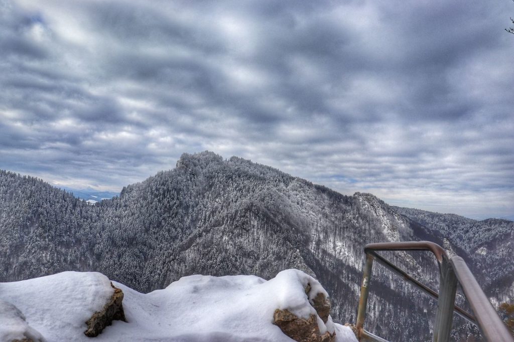 Widok rozciągający się z punktu widokowego na Sokolicy zimą, zachmurzone niebo, ośnieżone skały, metalowa barierka