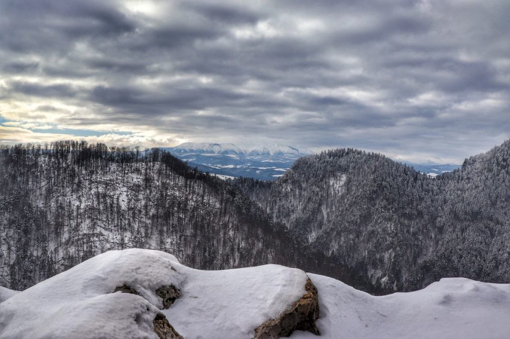 Widok ze szczytu Sokolica (Pieniny) na Tatry, skały pokryte śniegiem, na niebie ciemne chmury