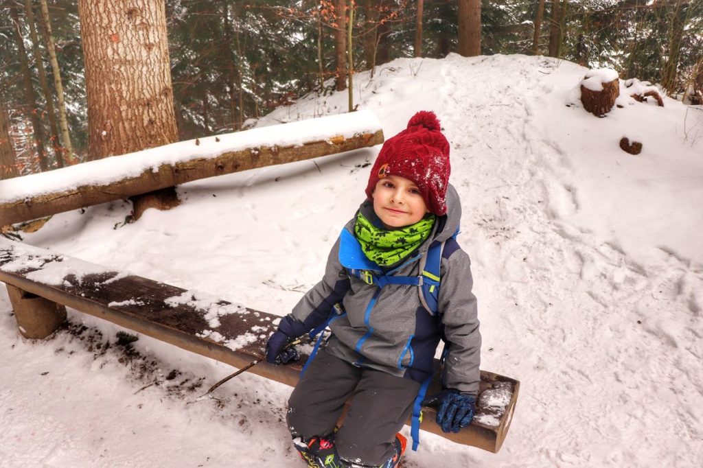 Zadowolone dziecko odpoczywające na drewnianej ławce na zielonym szlaku idącym na Sokolicę, las, zima