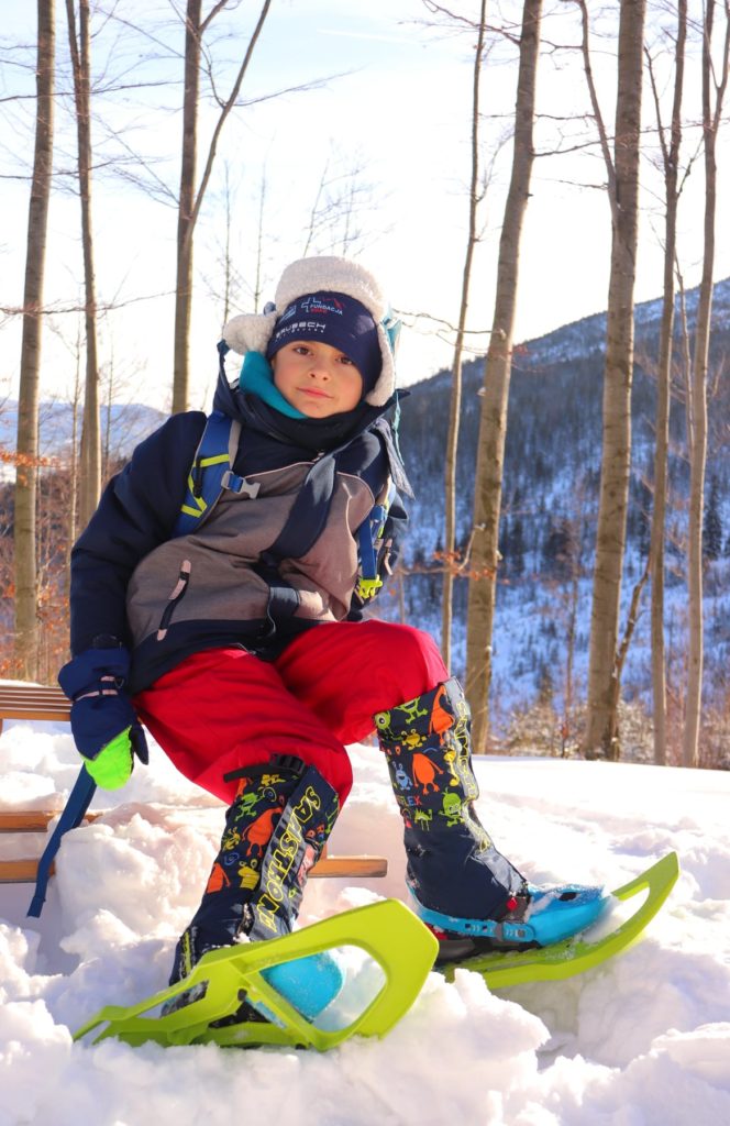 Zadowolone dziecko siedzące na drewnianych sankach w rakietach śnieżnych w drodze na Halę Baranią