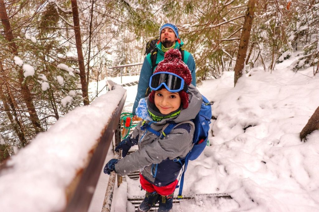 Zadowolone dziecko z tatą na metalowych schodach pokryrtch śniegiem - zielony szlak na Wysoką w Pieninach, droga leśna, zima