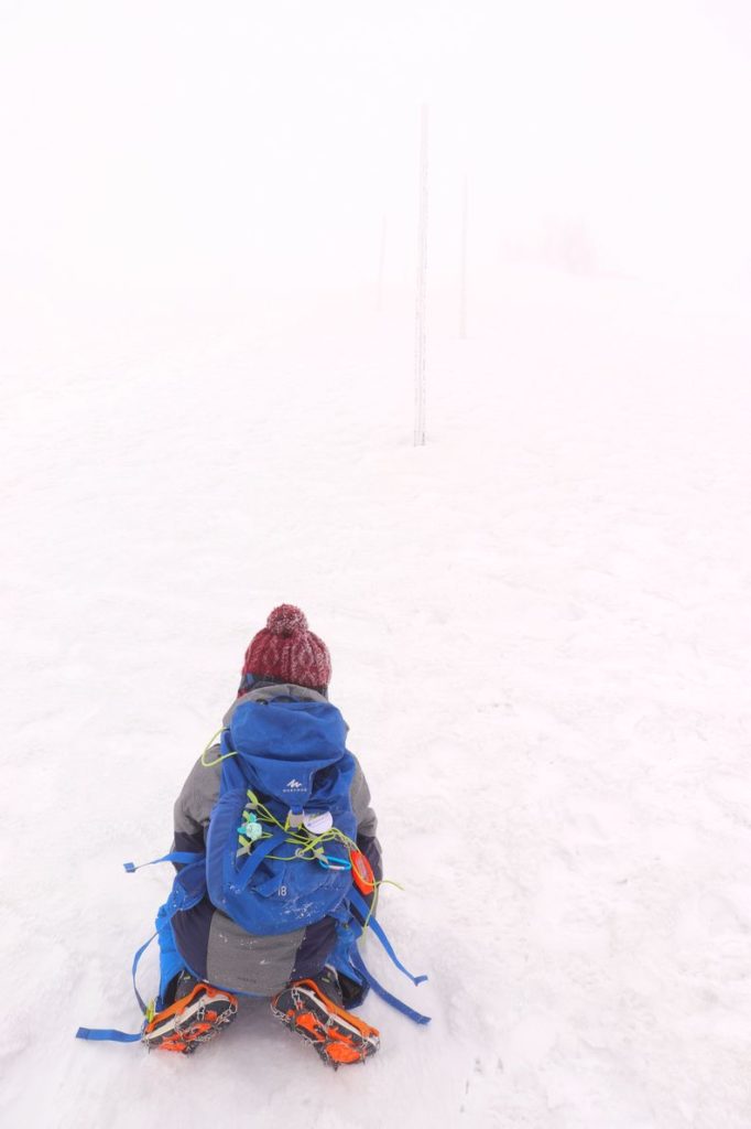 Dziecko na kolankach na szlaku prowadzącym w stronę Śnięznych Kotłów, ledwo widoczne przez mgłę drewniane tyczki