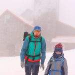 Turysta z dzieckiem, zimowe warunki, mgła, w tle budynek, w którym znajduje się Radiowo – telewizyjny Ośrodek Nadawczy Śnieżne Kotły